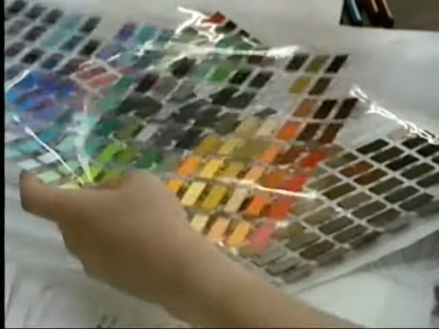 A person shuffling transparent sheets with dozens of 2x1 centimeter rectangular color samples.