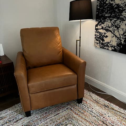 A small brown leather chair that is secretly a recliner tucked away in the corner of my living room, next to it an old brass lamp.